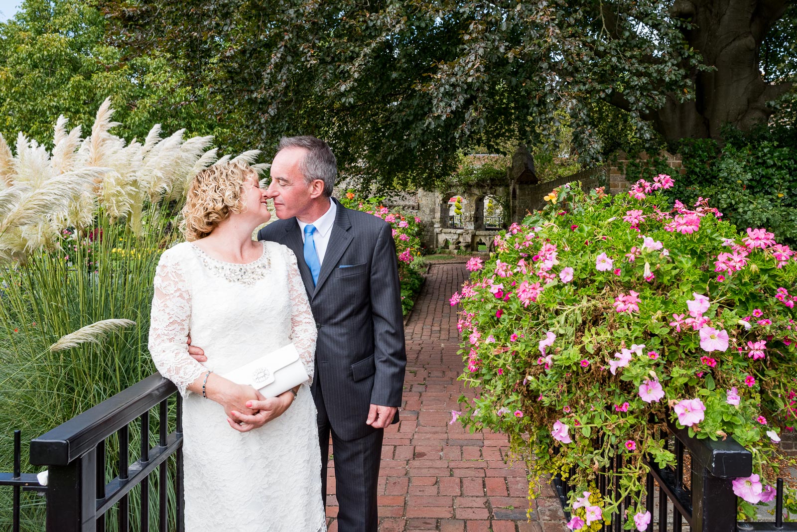 Wendy and Chris stand on the bridge among flowers in Southover Grange after their wedding at lewes Register Office.