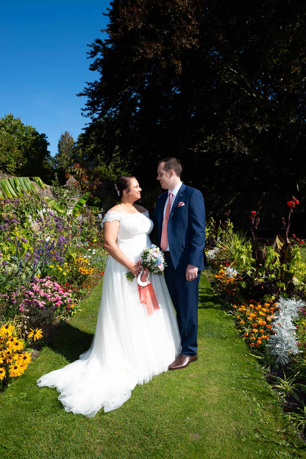 Amy and James look at eachother inbetween the blooming beds of Southover Grange after their wedding.