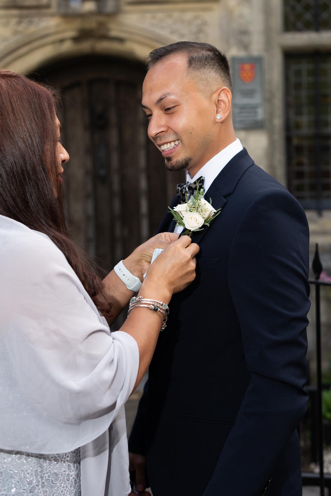 Jose mum pins attaches a wedding pin to his lapel outside Lewes Registry before his wedding to Ady. 