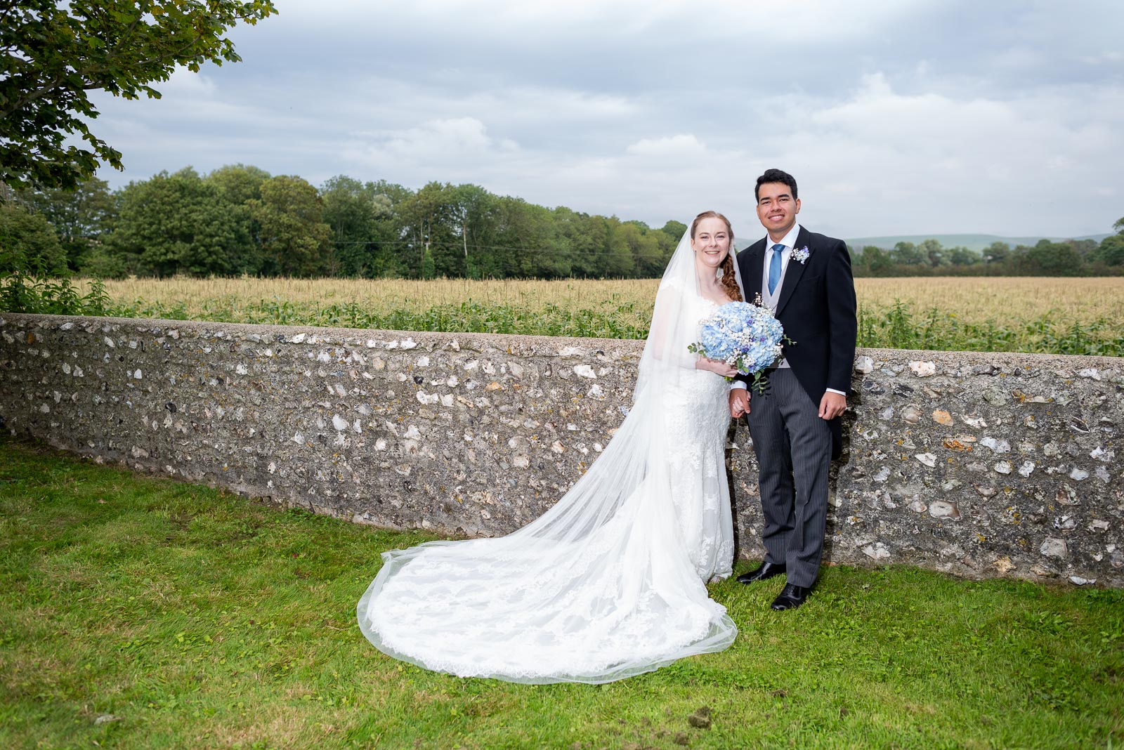 Lily and Callum pose with the downs in the background after getting married at St Nicholas Church in Iford.