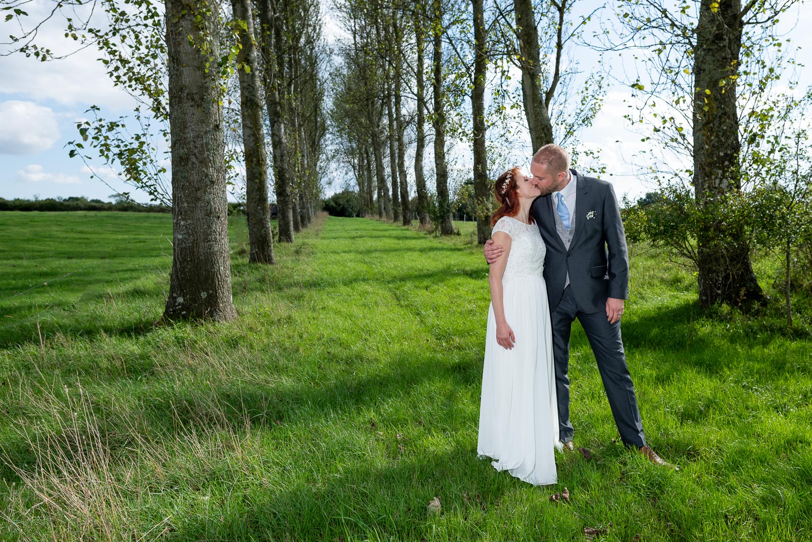 Adrienn and Lee embrace on front of a line of trees on the grounds of Milward Farm in Lewes after their Wedding on the estate.