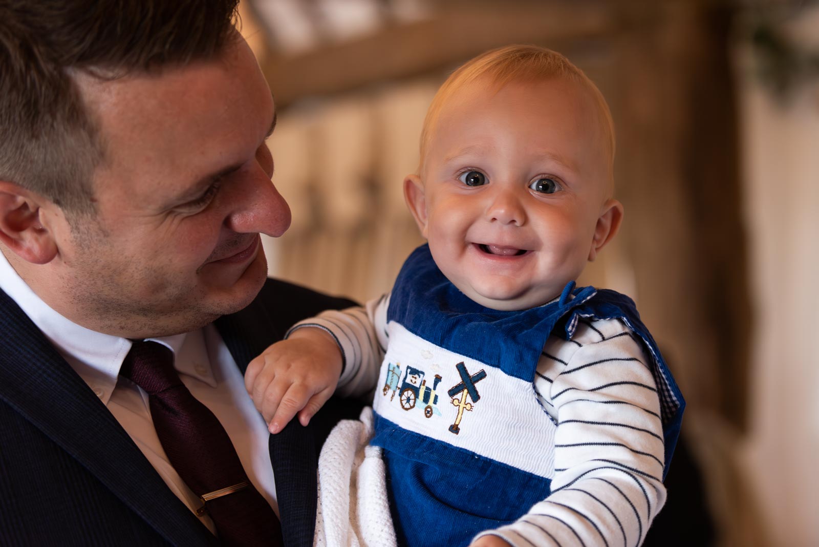 A six month old baby smiles in their dad's arms before Adrienn and Lee get married at Milwards Farm Estate near Lewes.