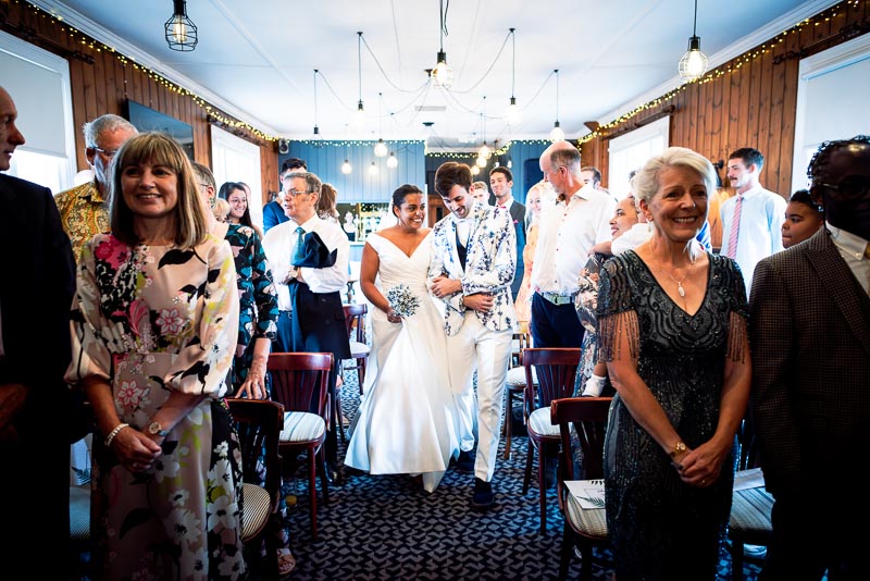 Olivia and Edward walking down the wedding aisle surrounded by guests at Th eRoyal Oak in Lewes.