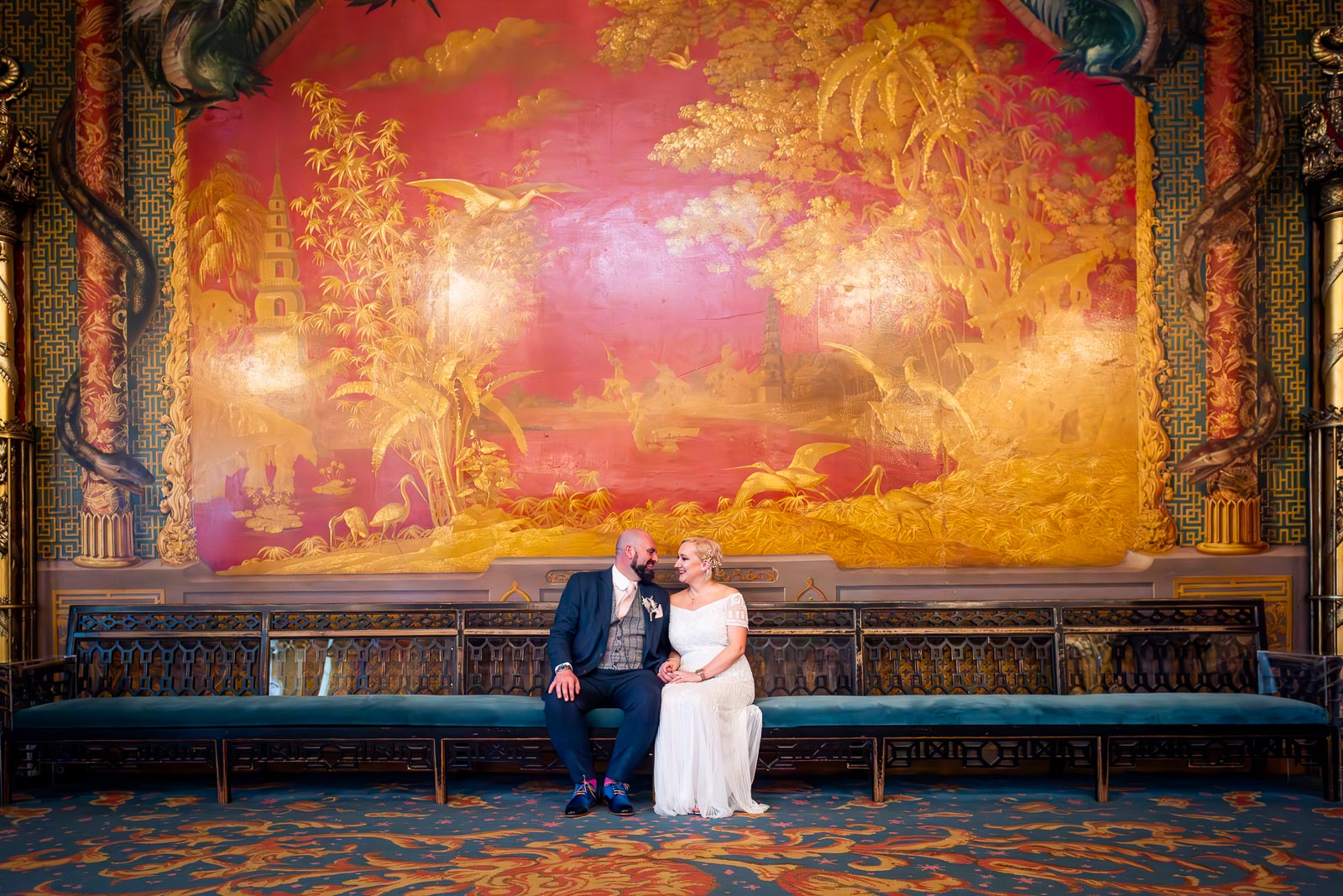 Georgina and Andy smile at each other on front of a huge painted fresco in The Music Room at Brighton Royal Pavilion.