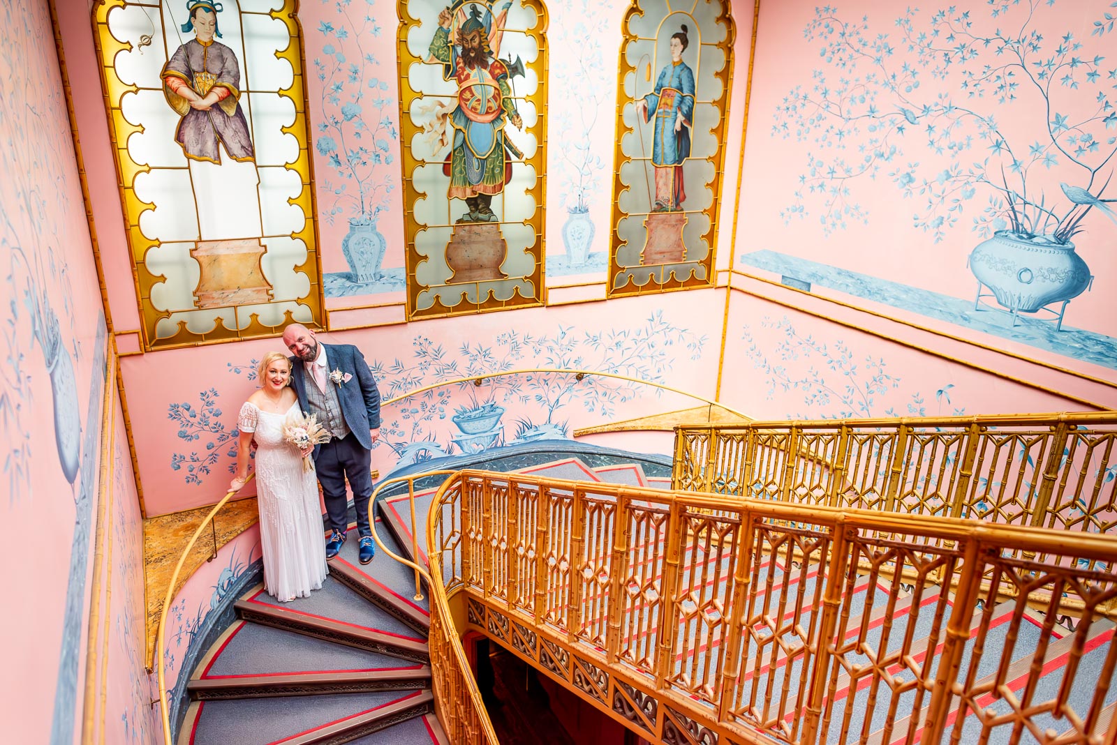 Georgina and Andy smile on the beautifully decorated Bamboo Stairs in Brighton Royal Pavilion after their wedding.