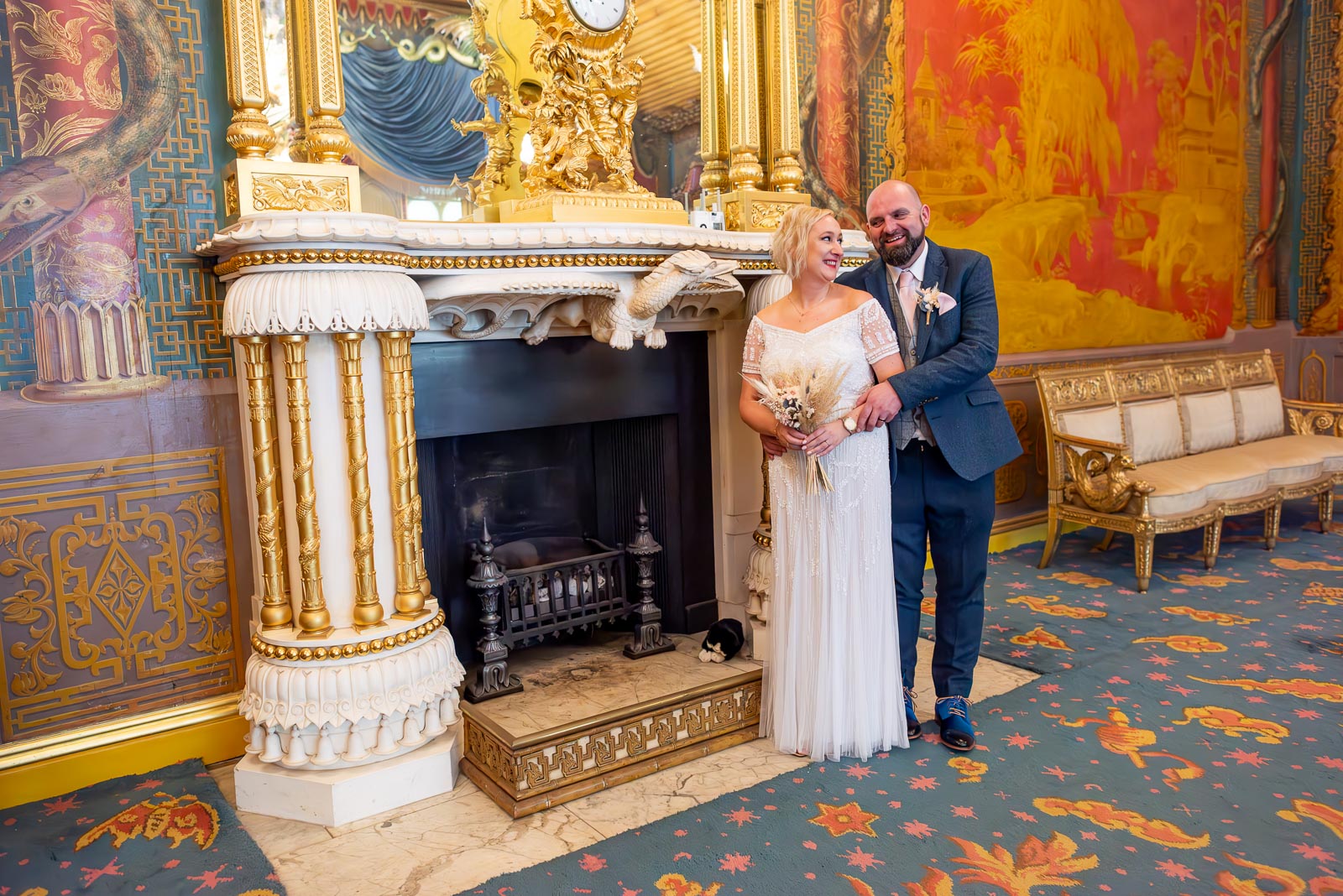 Georgina and Andy smile at each other on front of the ornate fireplace in The Music Room at Brighton Royal Pavilion.