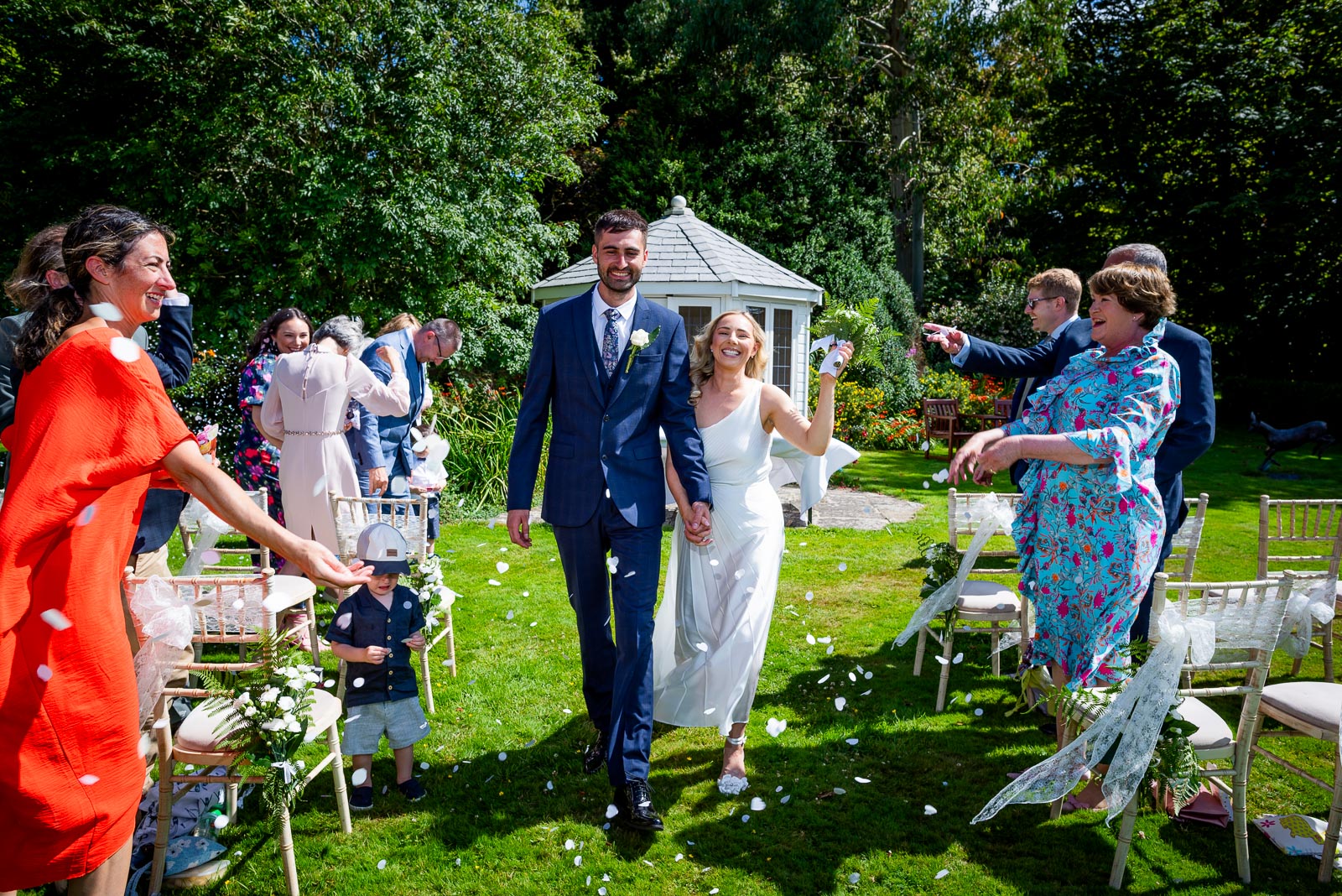 Jess and Fred walk through confetti after their wedding in the gardens at Horsted Place Hotel.